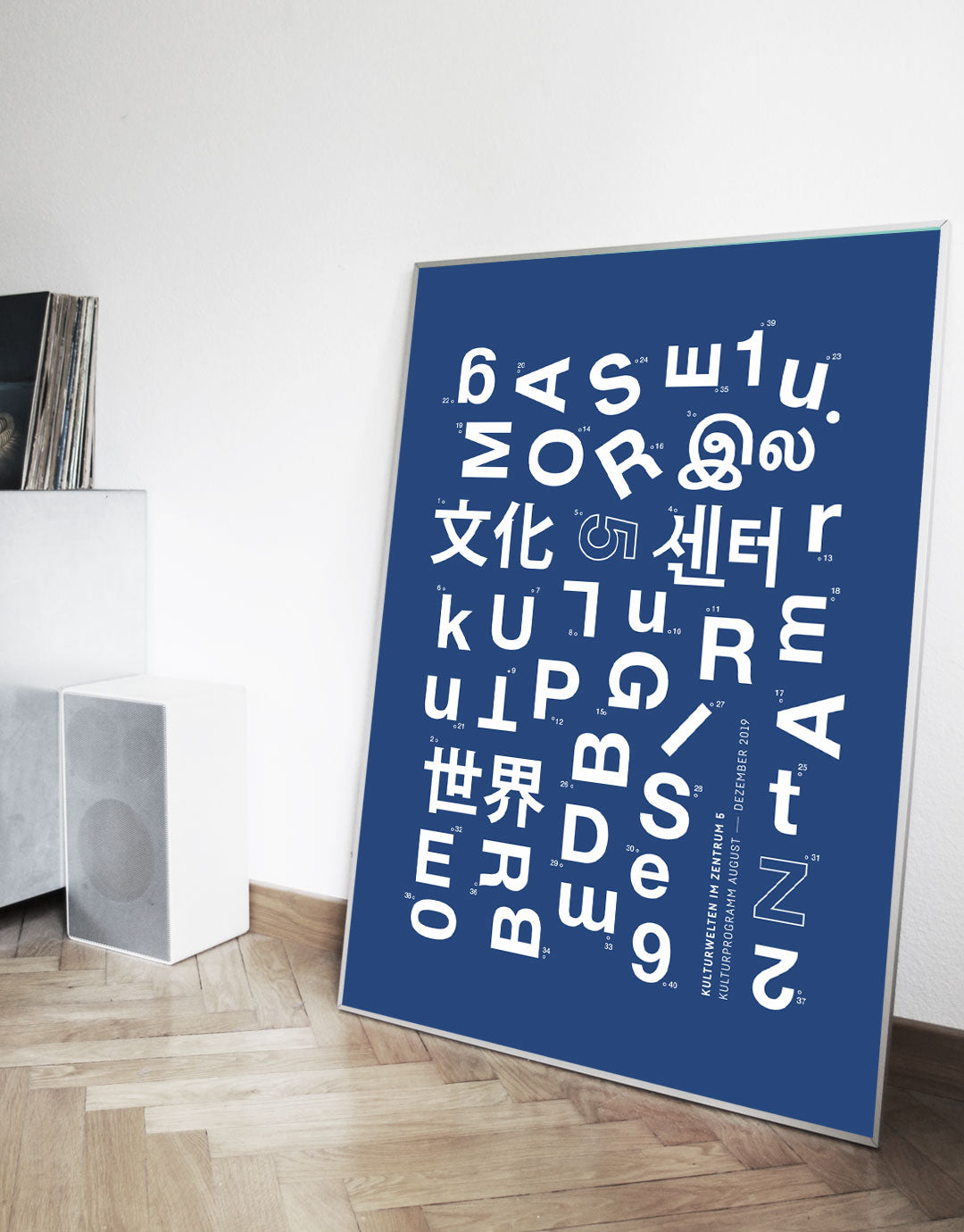 Poster mit einer kreativen Anordnung von Buchstaben und Zeichen in verschiedenen Sprachen auf einem blauen Hintergrund, das die Kulturwelten 2019 darstellt. Die Gestaltung kombiniert verschiedene Schriftarten und -stile, um ein modernes und dynamisches Kunstwerk zu schaffen, ideal für Liebhaber zeitgenössischer Grafiken und kultureller Themen.